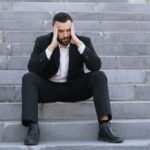 Un homme en costume, assis sur un escalier, la tête entre les mains.