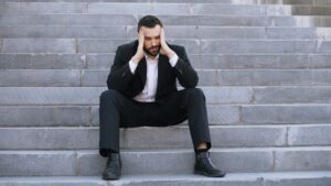 Un homme en costume, assis sur un escalier, la tête entre les mains.