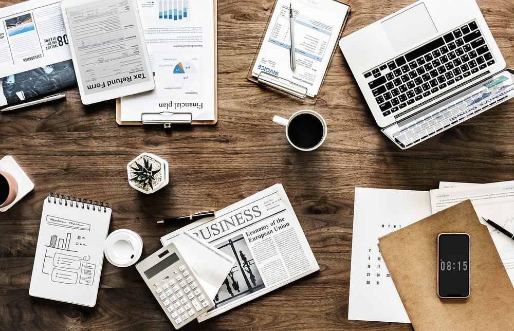 Espace de travail avec laptop, journaux financiers, documents et café sur bureau en bois Espace de travail avec laptop, journaux financiers, documents et café sur bureau en bois