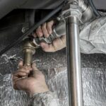 Des mains serrent une tuyauterie métallique sous un évier