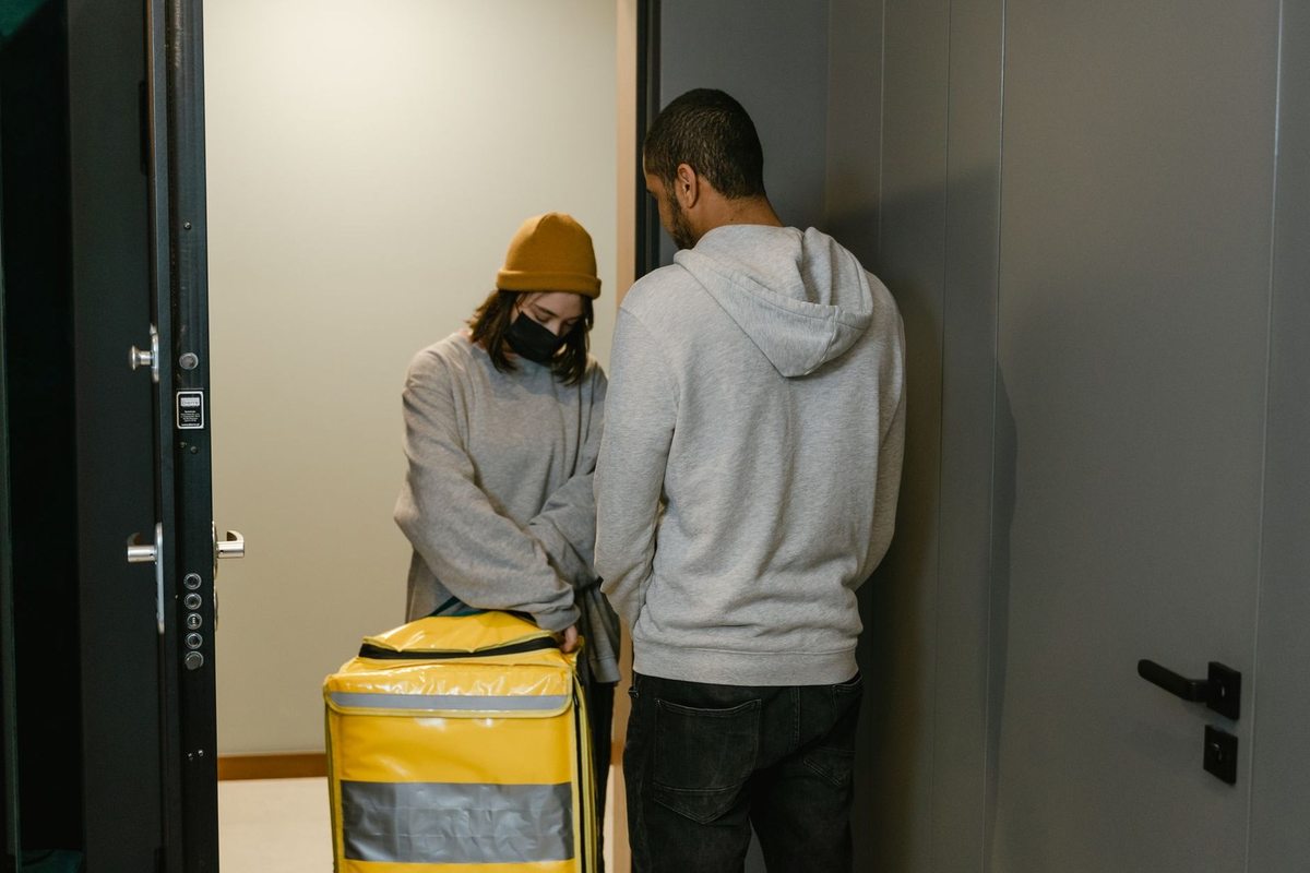 Deux individus devant une porte, l'un portant un sac jaune avec une étiquette, l'autre observant Deux individus devant une porte, l'un portant un sac jaune avec une étiquette, l'autre observant